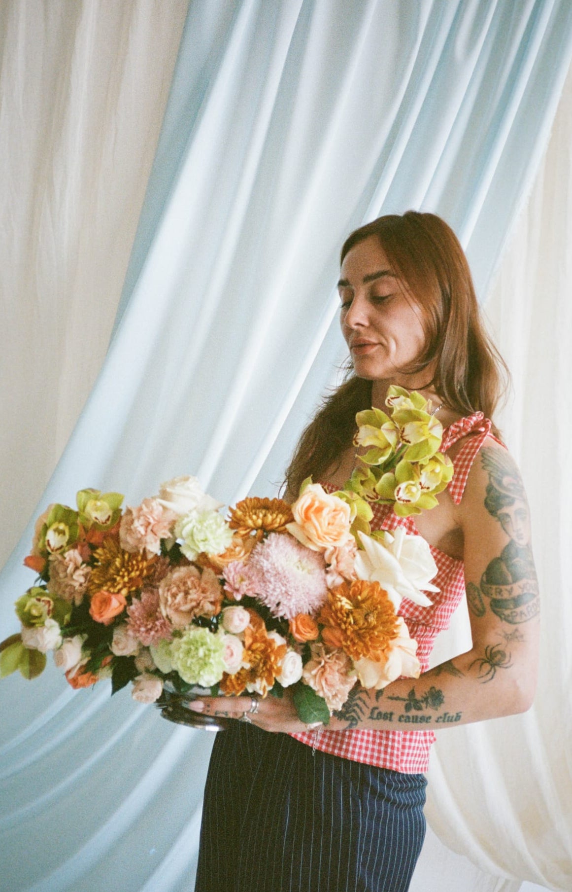 Woman holding a large bouquet of flowers in front of white curtains